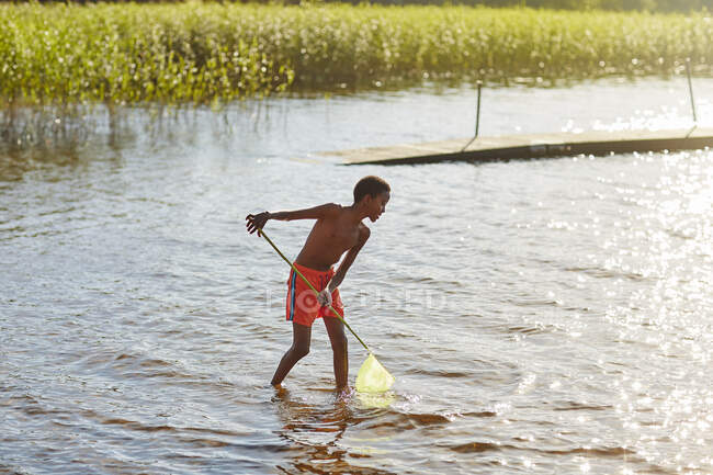 Boy playing with net on lake — Stockfoto