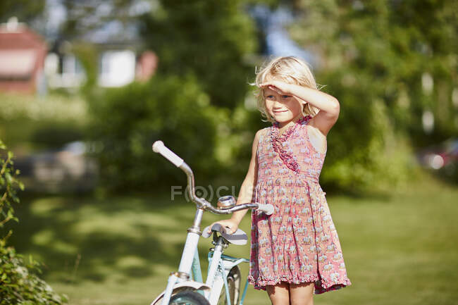 Girl with bicycle shielding her eyes — Photo de stock