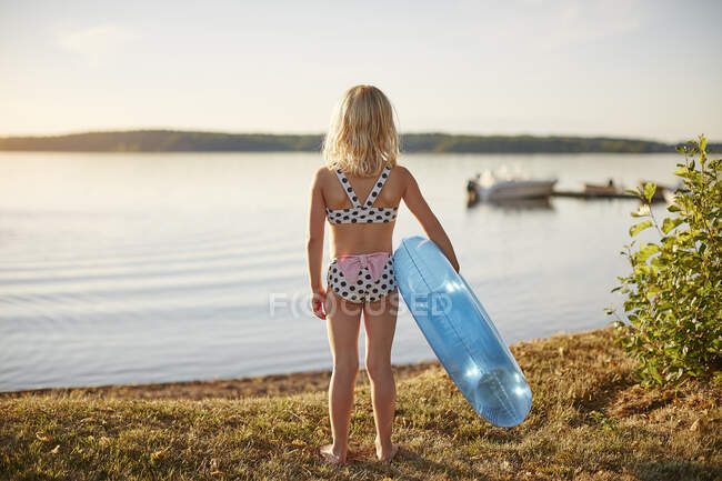 Fille en maillot de bain avec jouet gonflable par lac au coucher du soleil — Photo de stock