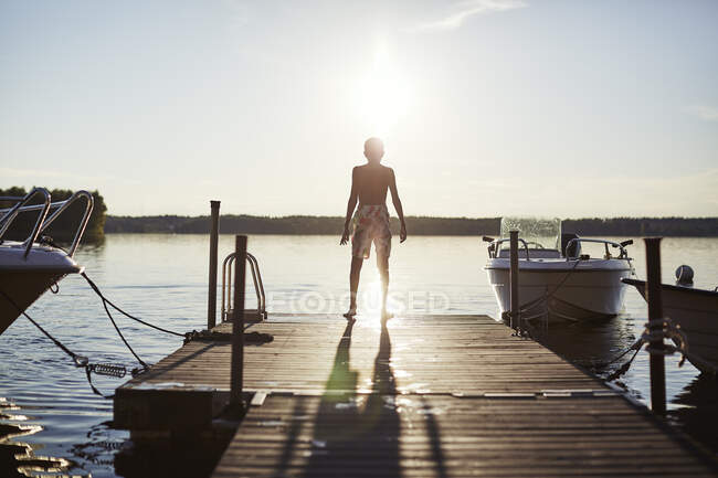 Junge in Badehose steht bei Sonnenuntergang auf Steg am See — Stockfoto