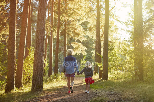 Madre e hija caminando en el bosque al atardecer - foto de stock