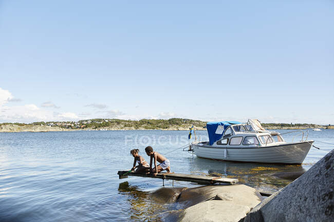 Siblings by boat playing on lake jetty — Fotografia de Stock