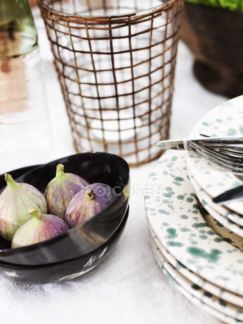 Bowl of figs by stack of plates — Stock Photo