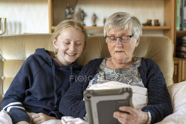 Девушка и ее бабушка используют планшетный компьютер на диване — стоковое фото