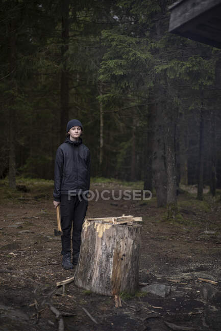 Adolescente menino segurando machado por toco de árvore — Fotografia de Stock