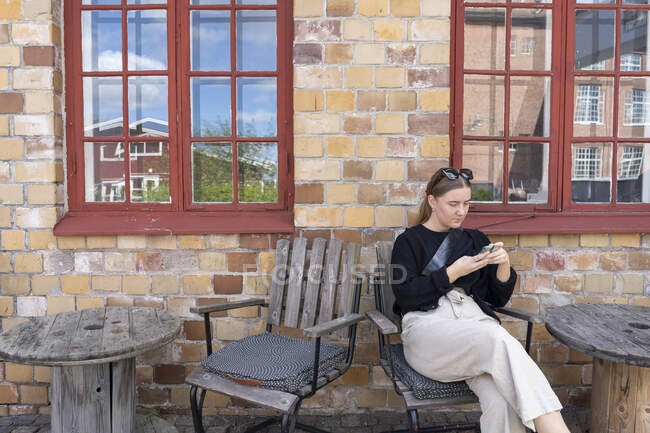 Jovem mulher usando telefone inteligente na cadeira de madeira — Fotografia de Stock