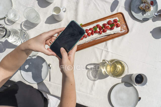 Hands of teenage girl taking photograph of strawberry dessert — Stock Photo