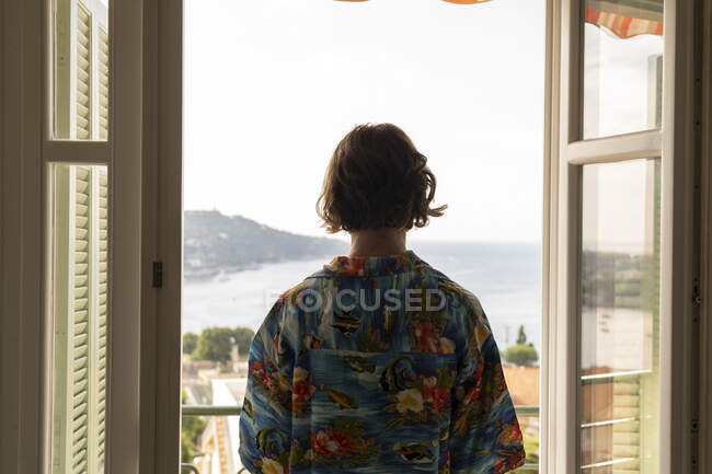 Vue arrière du garçon adolescent en chemise colorée sur le balcon — Photo de stock