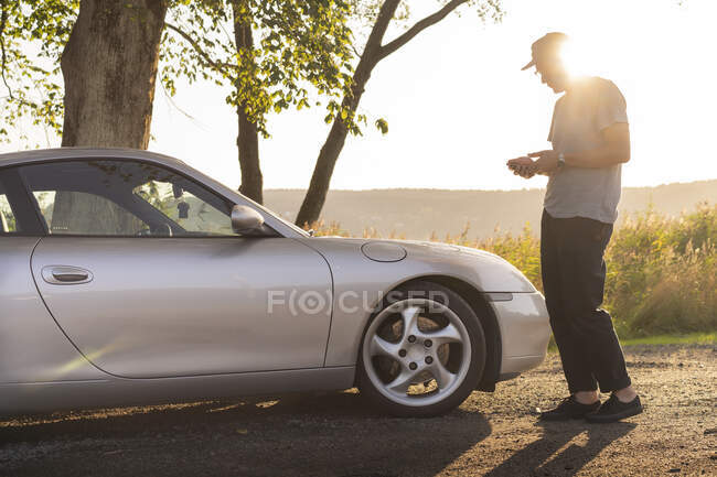 Man using smart phone by sports car at sunset — Foto stock