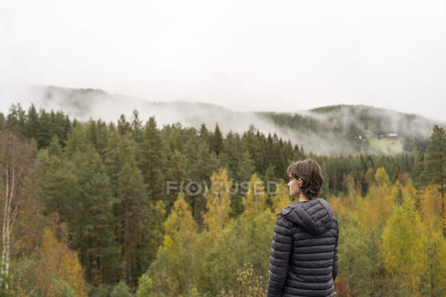 Мальчик-подросток смотрит на осенний лес — стоковое фото