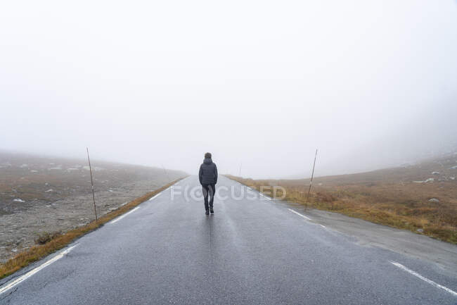 Adolescente de casaco andando na estrada nebulosa — Fotografia de Stock