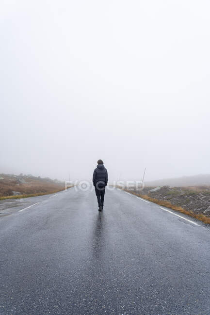 Adolescente de casaco andando na estrada nebulosa — Fotografia de Stock
