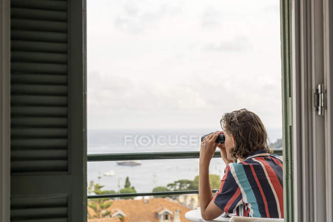 Jeune garçon en chemise rayée regardant à la mer avec des jumelles — Photo de stock