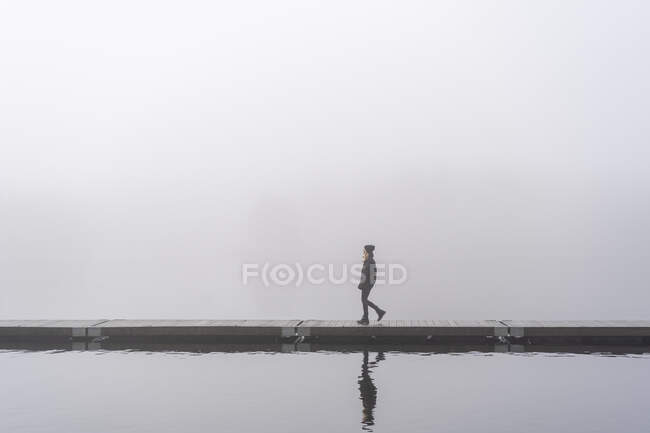 Teenage girl walking on jetty on lake under fog — Stockfoto