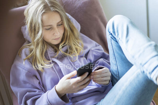 Teenagermädchen in lila Kapuzenpulli sendet SMS auf Smartphone — Stockfoto