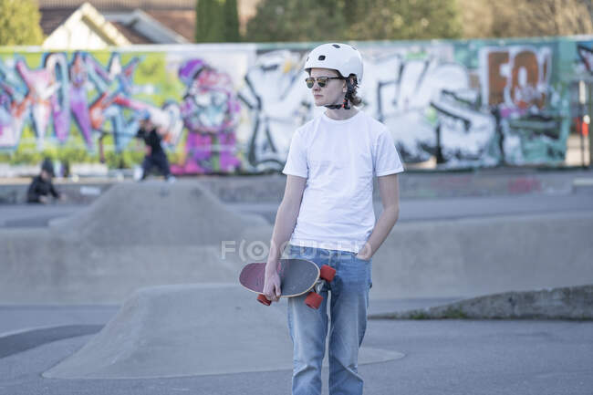Молодой человек в шлеме и скейтборде в скейт-парке — стоковое фото