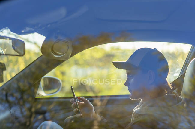 Young man using smart phone through car window — Fotografia de Stock