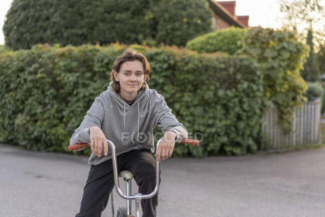 Молодой человек в капюшоне сидит на велосипеде — стоковое фото