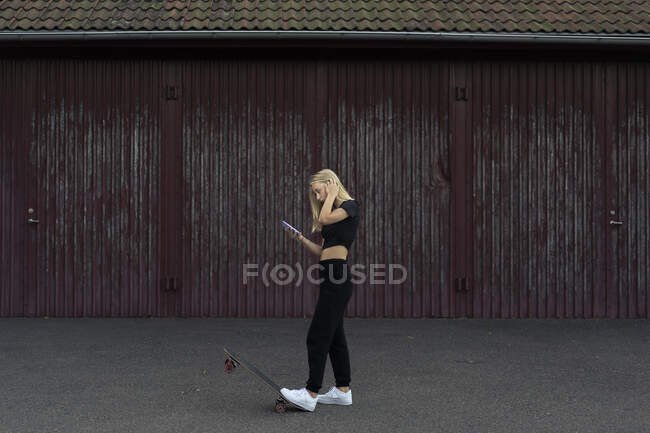 Teenage girl holding smart phone while skateboarding — Stock Photo