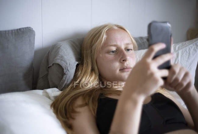 Teenage girl text messaging on bed - foto de stock