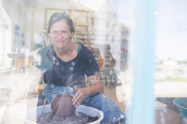 View through window of potter using pottery wheel - foto de stock