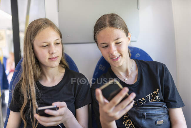 Sisters with smart phones commuting on train - foto de stock