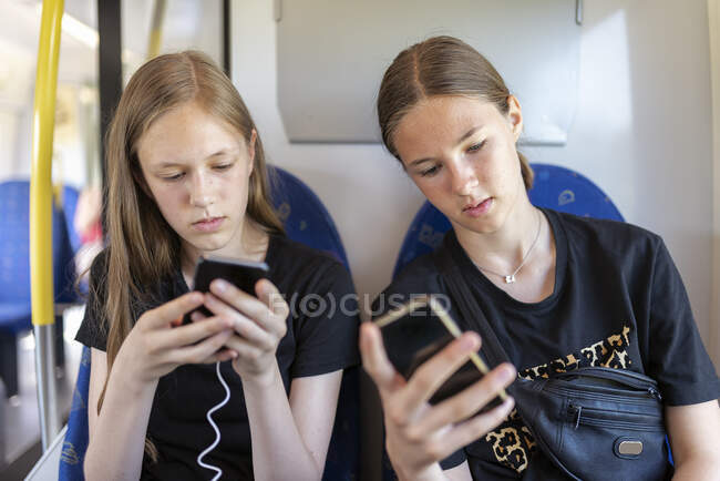 Hermanas con teléfonos inteligentes viajando en tren - foto de stock