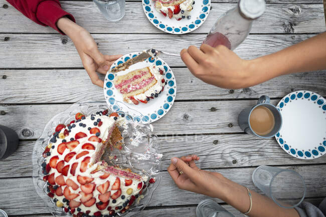 Hands of boy and young woman serving berry cake — Stock Photo
