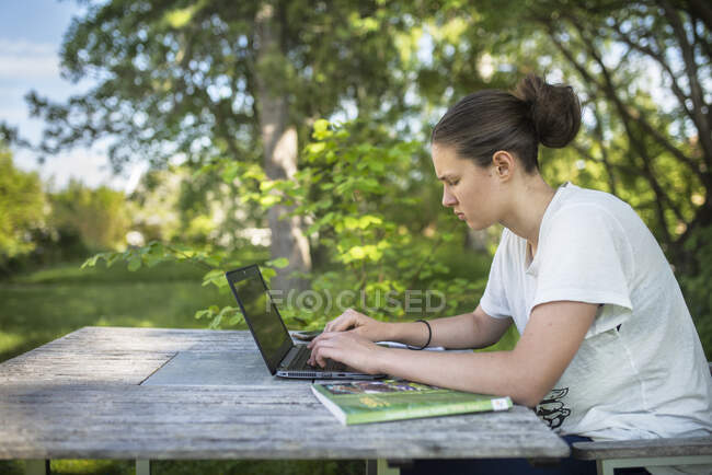 Teenage girl doing homework on laptop at outdoor table — Stock Photo
