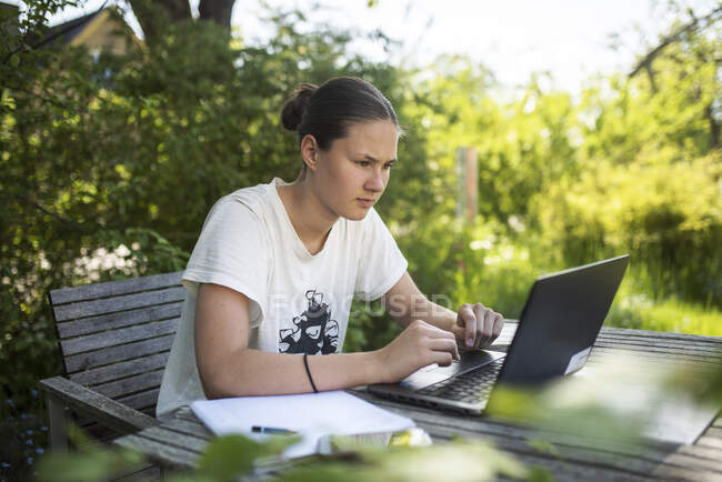 Дівчина-підліток робить домашнє завдання на ноутбуці на відкритому столі — стокове фото