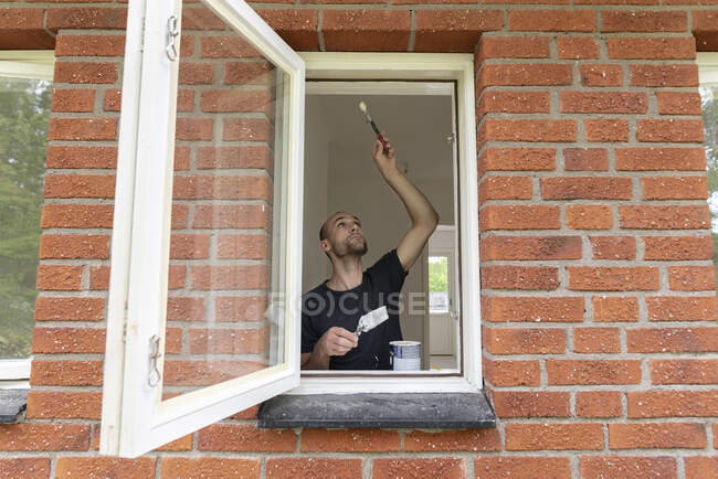 Homme peinture par la fenêtre de la maison — Photo de stock