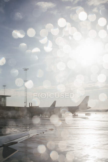 Airplanes at airport through window at sunset — Stock Photo