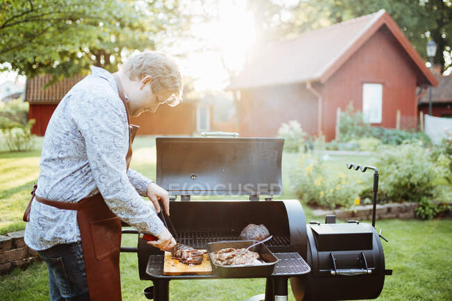 Jeune homme cuisinant de la viande sur barbecue — Photo de stock