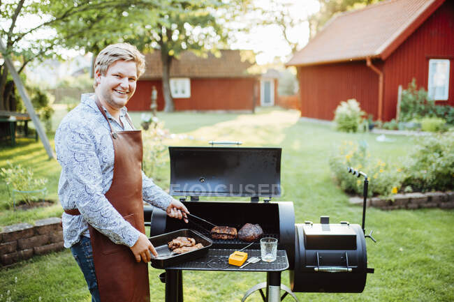 Giovane uomo che cucina carne sul barbecue — Foto stock