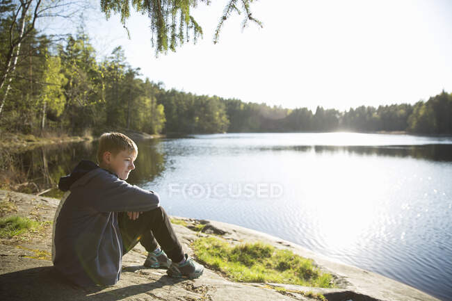 Niño sentado junto al lago Trehorningen en la Reserva Natural de Domarudden, Suecia - foto de stock