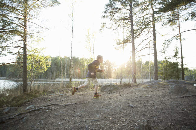 Boy running by Trehorningen Lake in Domarudden Nature Reserve, Sweden - foto de stock