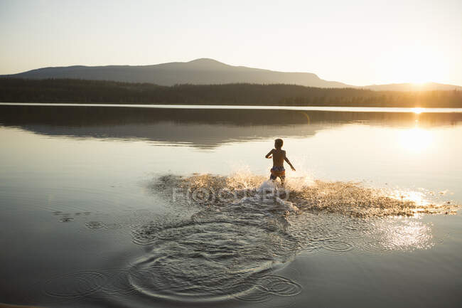 Chico salpicando en el lago Ottsjo al atardecer en la Reserva Natural de Valadalen, Suecia - foto de stock