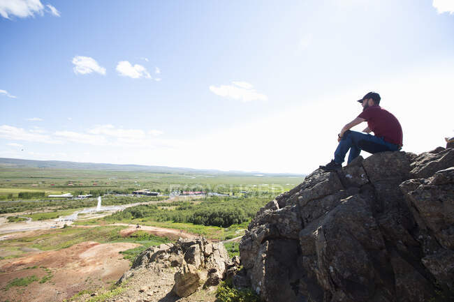 Зрелый мужчина смотрит на вид, сидя на скале — стоковое фото
