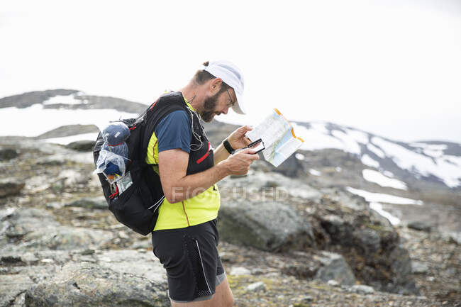 Mature man looking at map and compass on mountain — Stockfoto