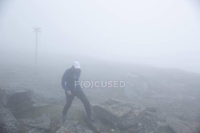 Homem maduro caminhando sobre rochas na montanha nebulosa — Fotografia de Stock