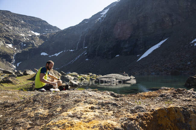 Mature man sitting by mountain lake — Foto stock
