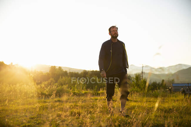 Homme mûr marchant dans le champ au coucher du soleil — Photo de stock