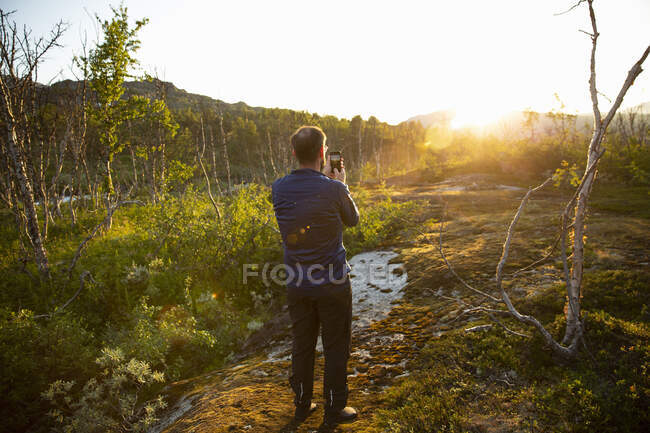 Зрілий чоловік фотографує захід сонця зі смартфоном — стокове фото