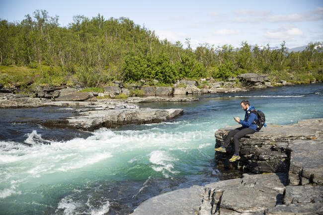L'uomo riposa sulla roccia lungo il fiume durante l'escursione — Foto stock