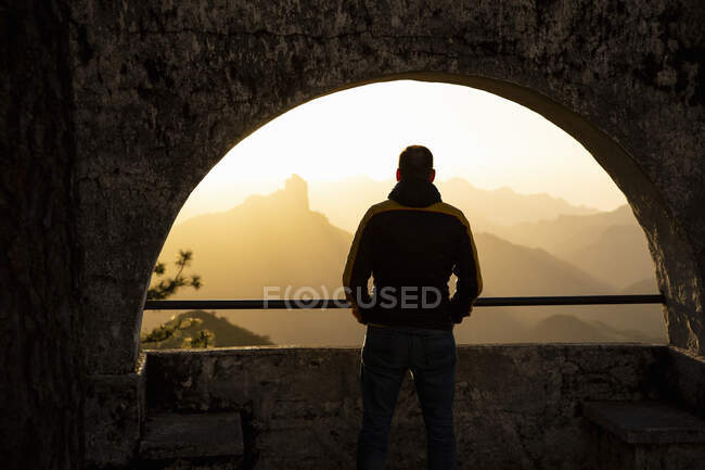 Чоловік стоїть біля арочного вікна на заході сонця — стокове фото