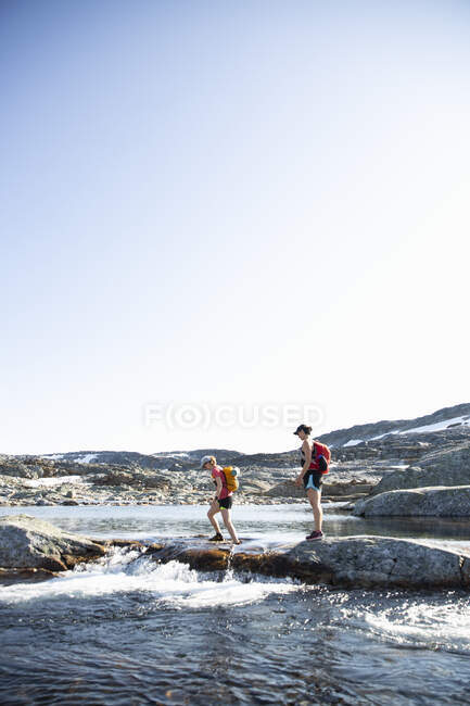 Women walking on rocks across river — Foto stock