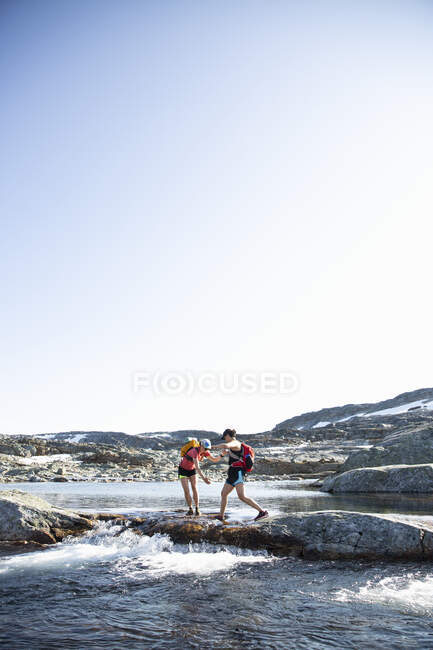 Women walking on rocks across river - foto de stock