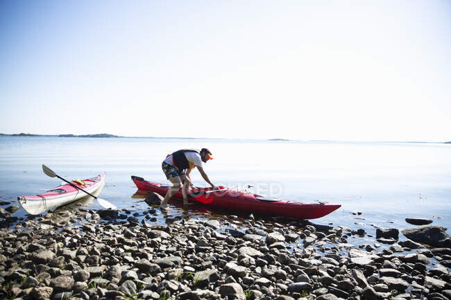 Homme avec kayak sur galets par la mer — Photo de stock