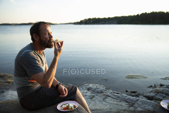 Homem tomando café da manhã por lago ao nascer do sol — Fotografia de Stock