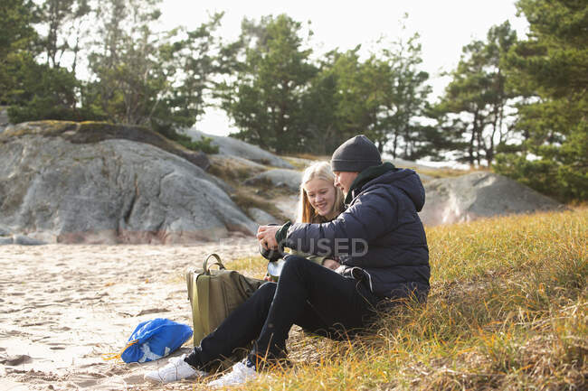 Padre e hija sentados en la hierba por la playa - foto de stock
